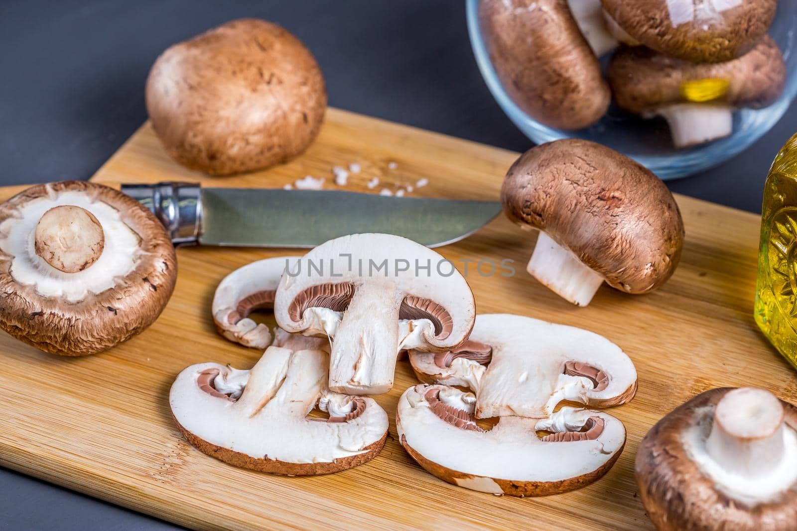 Royal champignons, Parisian champignons, chopped mushrooms on bamboo wooden chopping board, close-up. Dark wooden background. Side view.