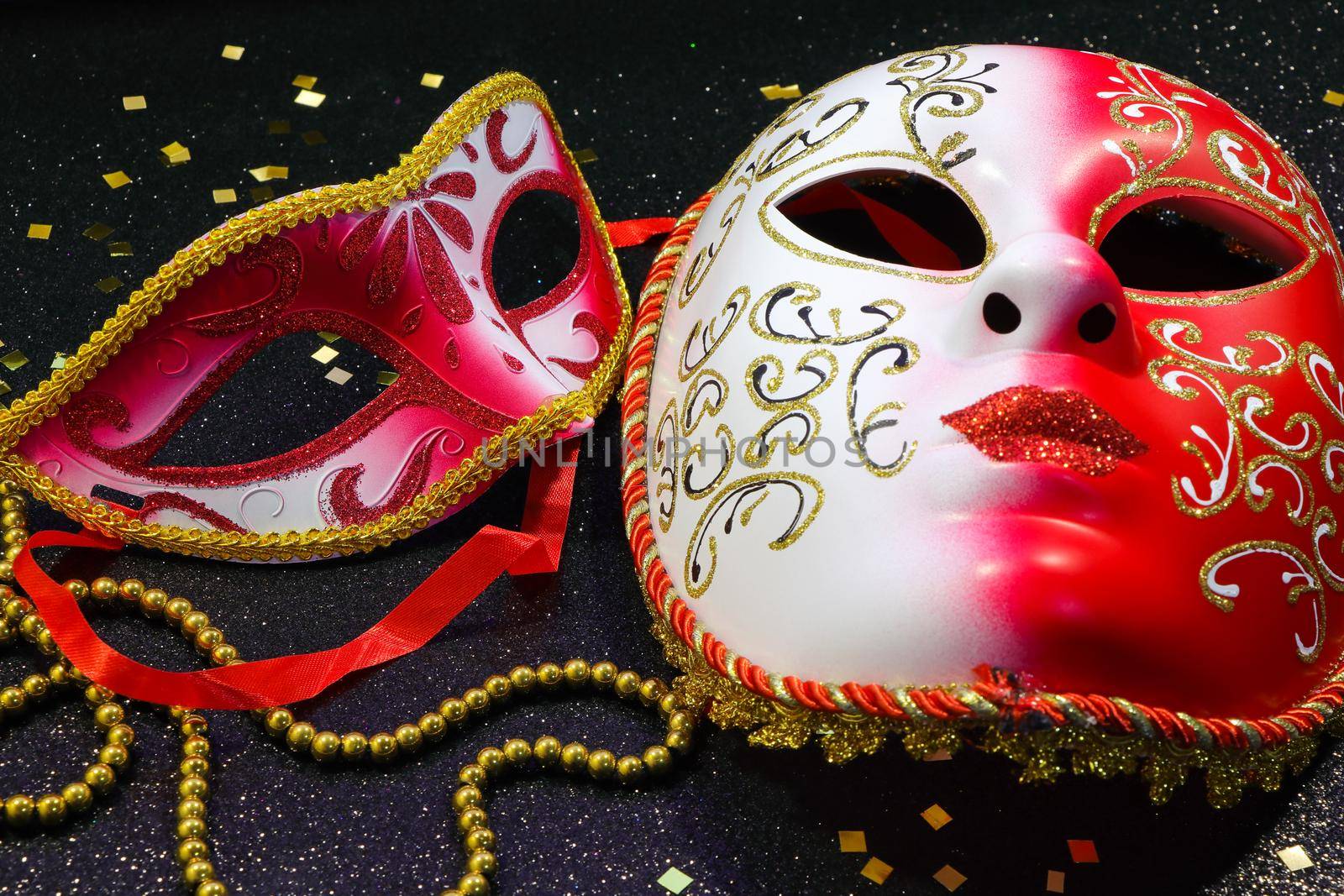 Mardi Gras red and white carnival face masks with gold confetti and bead string on textured black