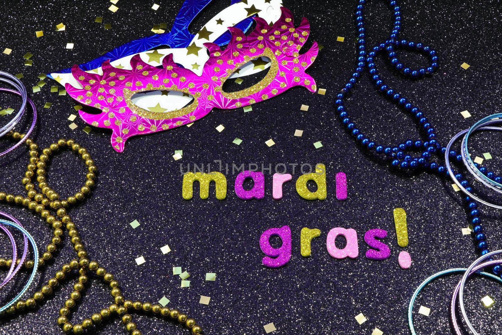 Mardi Gras text and confetti with party masks and jewelry on textured black