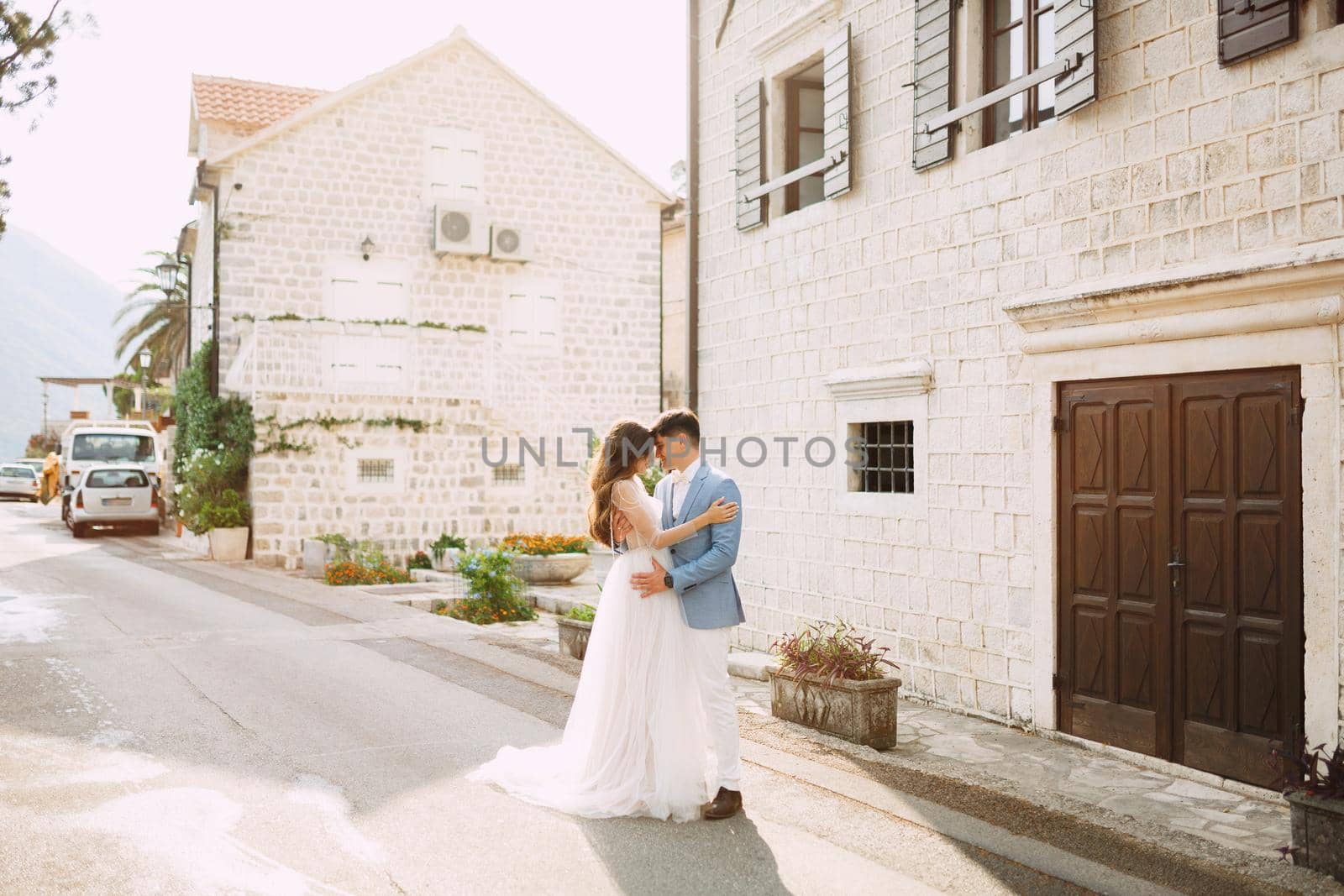 The bride and groom are embracing near the beautiful white houses in the old town of Perast . High quality photo