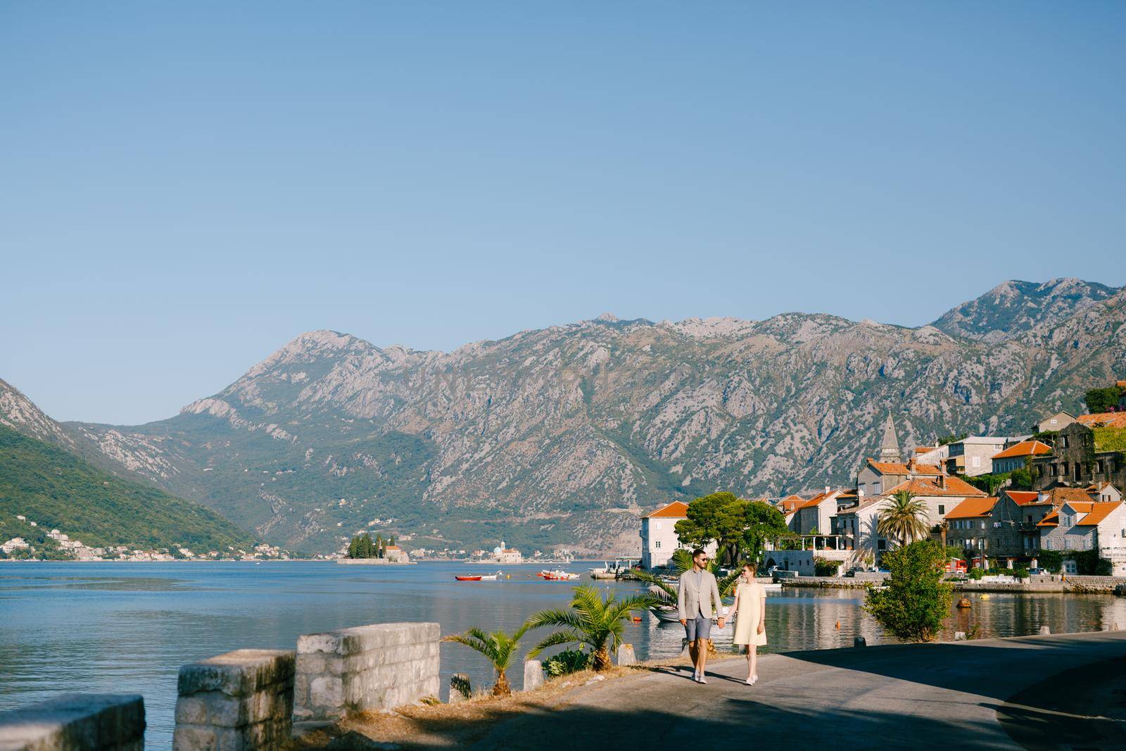A loving couple walks holding hands along the embankment of the old town of Perast by Nadtochiy