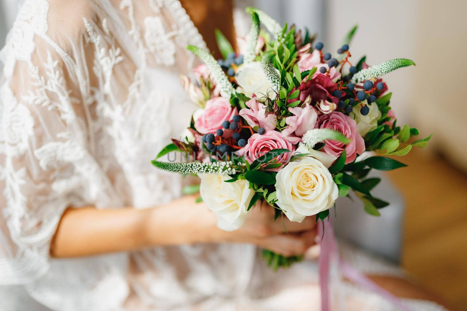 A bride in a white lace peignoir holds a wedding bouquet in her hands in a hotel room while preparing for a wedding ceremony by Nadtochiy