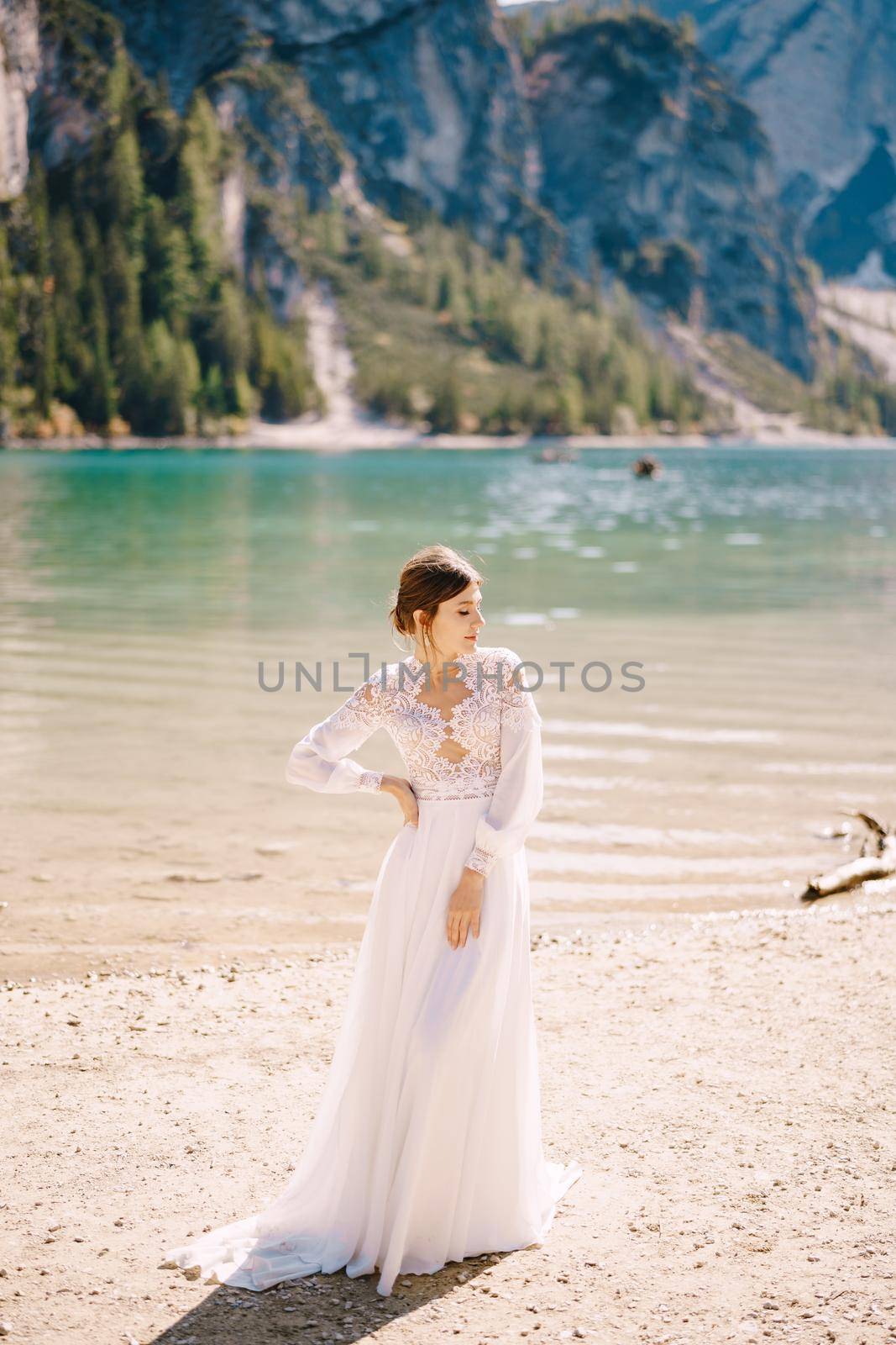 A beautiful bride in a white chiffon dress with sleeves and lace on the shores of Lake Lago di Braies in Italy. Destination wedding in Europe, on the popular Braies lake.