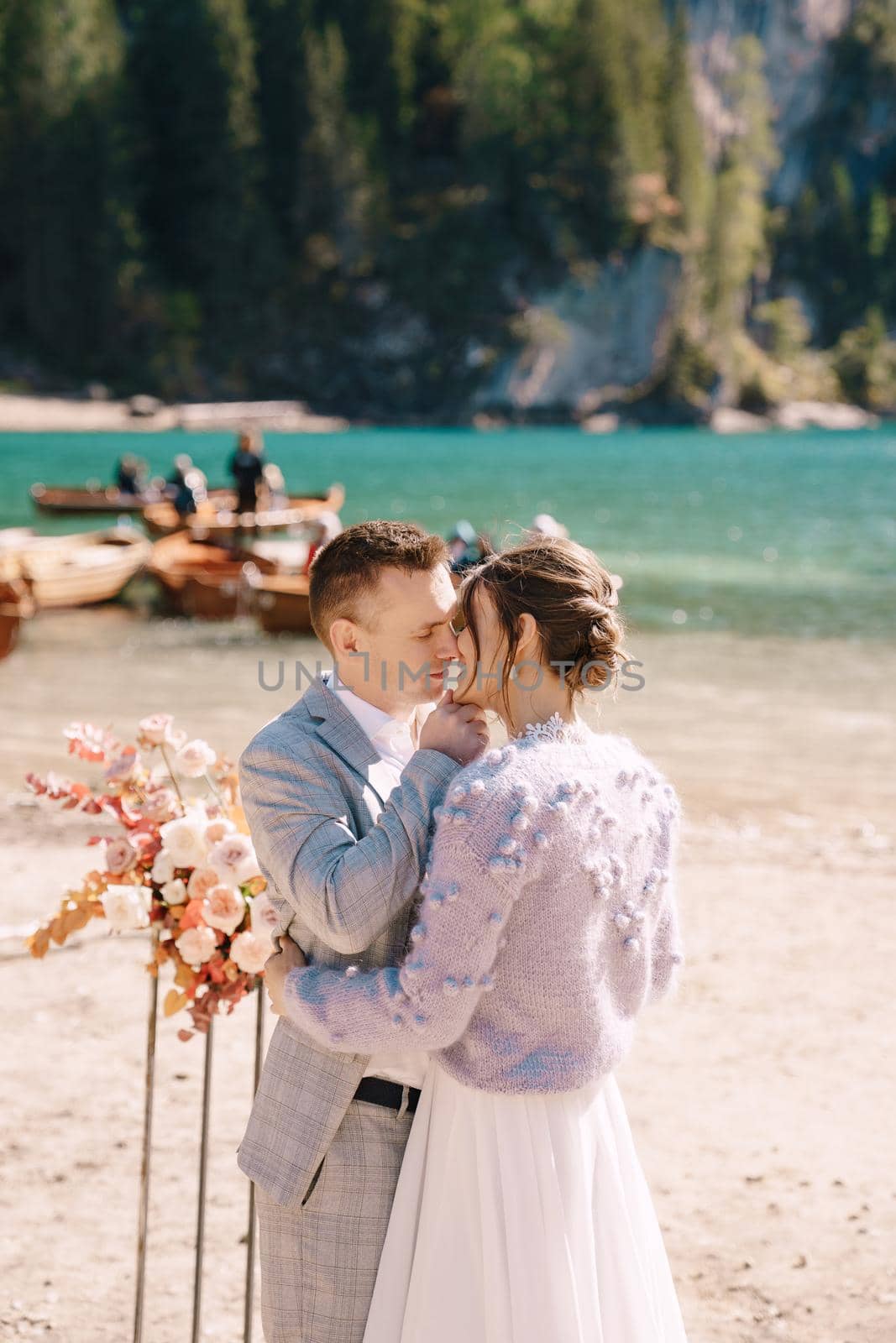 The groom dons a bride's ring, in place for the ceremony, with an arch of autumn floral columns, against the backdrop of Lago di Braies in Italy. Destination wedding in Europe, at Braies lake.