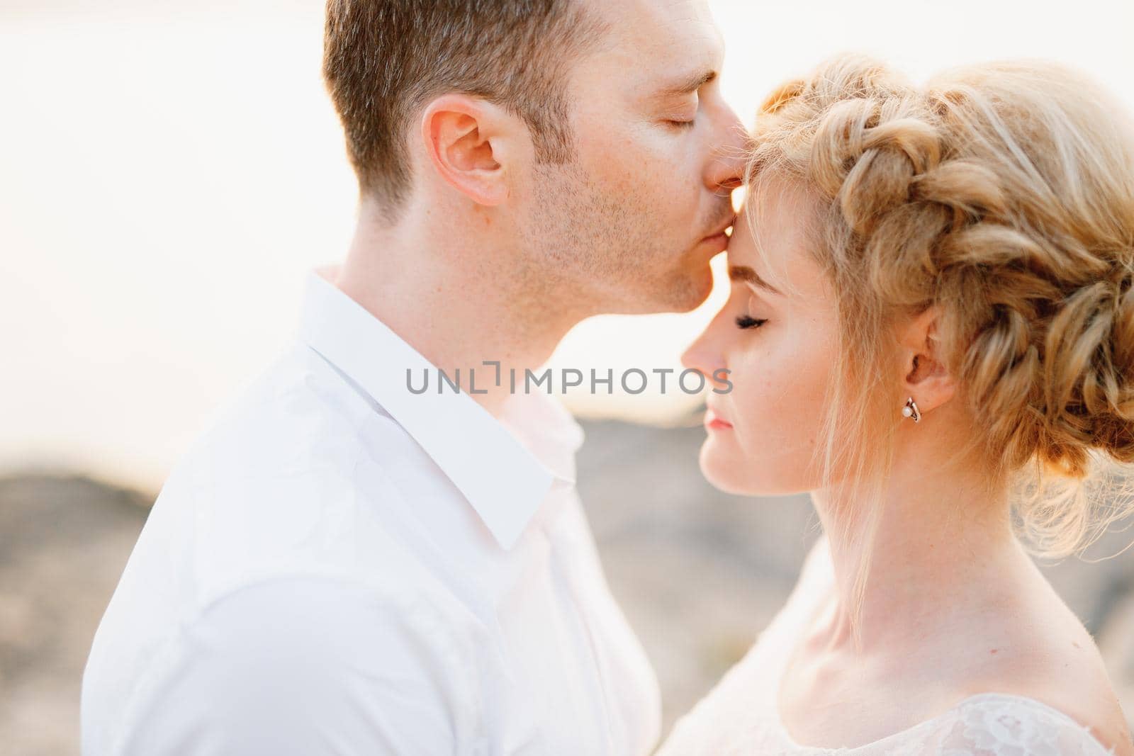 The groom gently kisses the bride on the forehead on the rocks by the sea, close-up. High quality photo