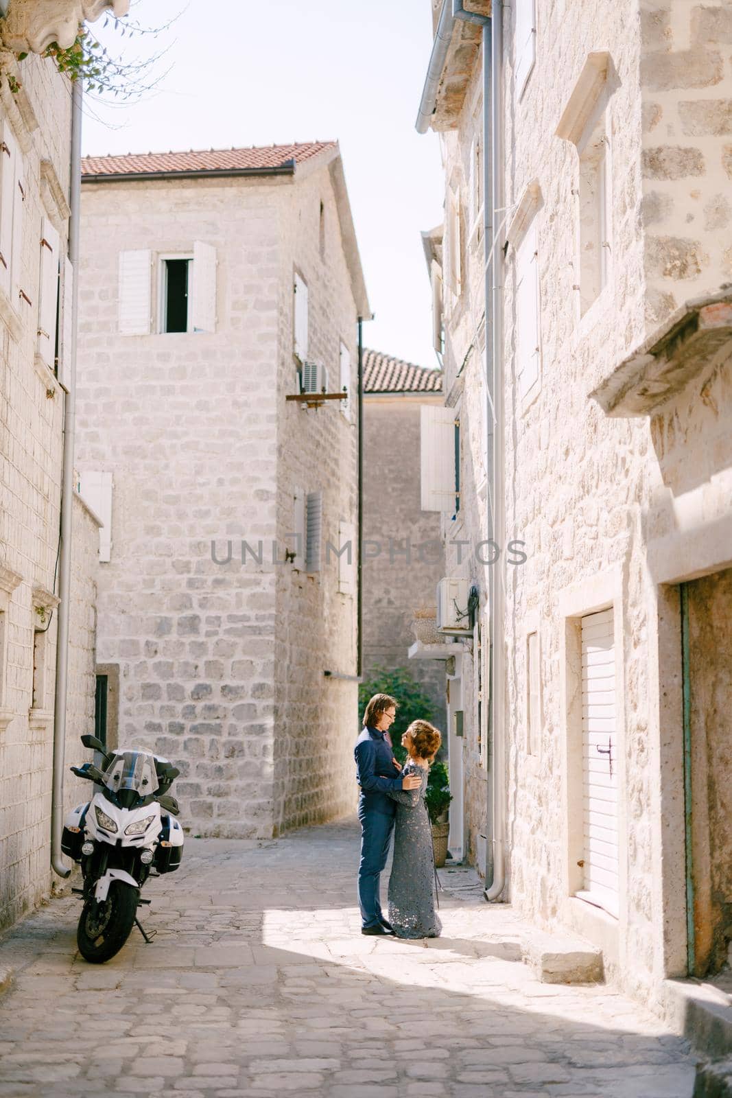 Bride in stylish blue dress and the groom hugging against the background of beautiful white houses in the old town of Perast, . High quality photo