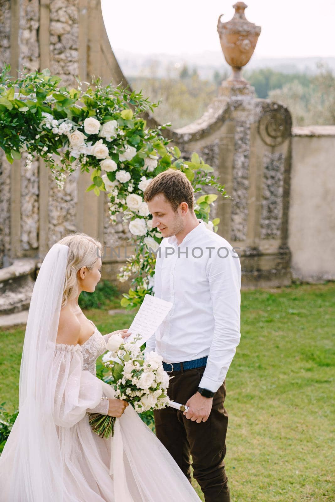Florence, Italy - 02 october 2019: Wedding at an old winery villa in Tuscany, Italy. The bride reads the wedding oath. Round wedding arch decorated with white flowers and greenery by Nadtochiy