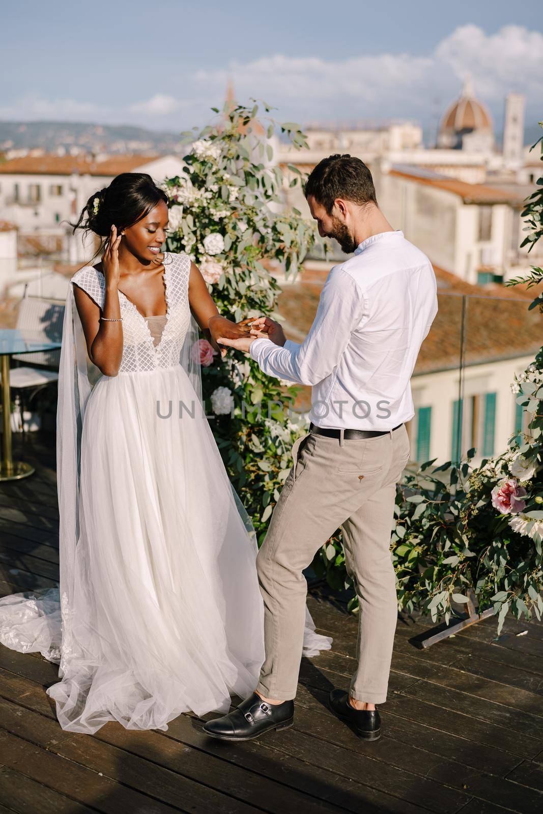 Interracial wedding couple. Destination fine-art wedding in Florence, Italy. A wedding ceremony on the roof of the building, with cityscape views of the city and Cathedral of Santa Maria Del Fiore