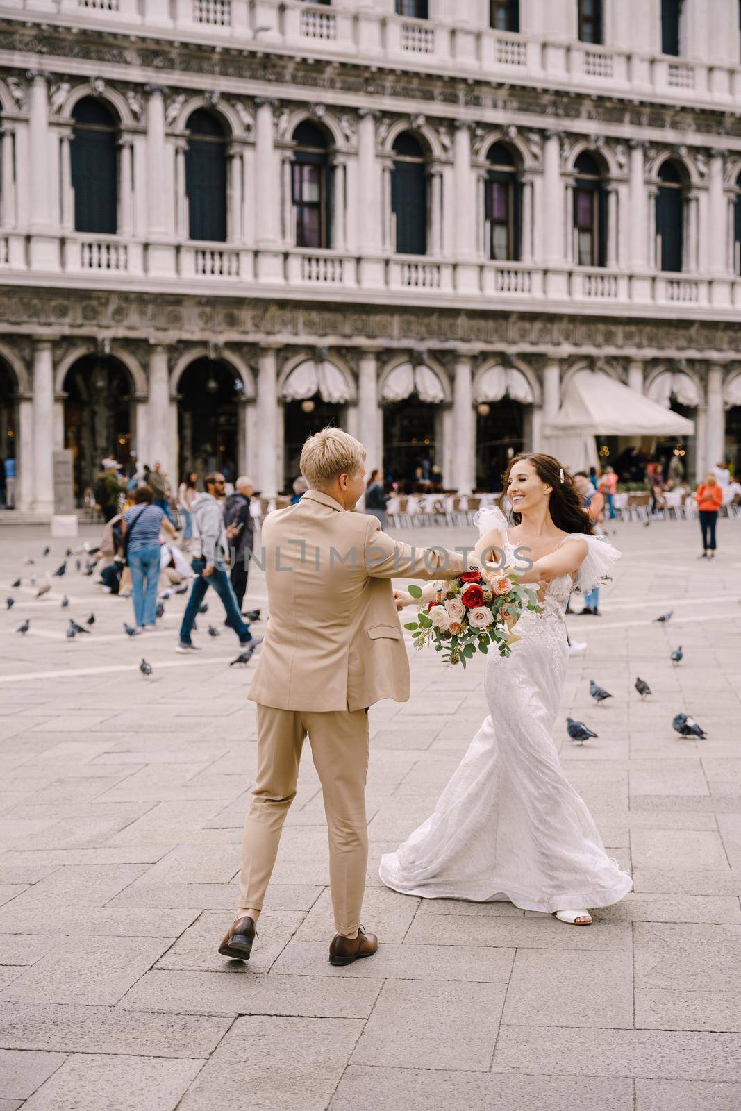 Venice, Italy - 04 october 2019: Wedding in Venice, Italy. The bride and groom are dancing among the many pigeons in Piazza San Marco, against the backdrop of National Archaeological Museum Venice by Nadtochiy