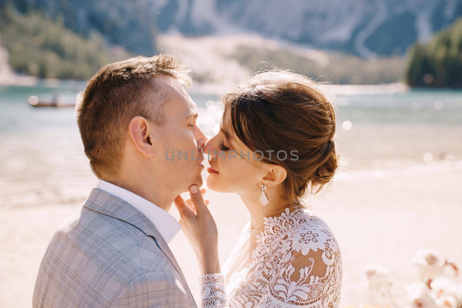 Newlyweds kiss on the spot for the ceremony, with an arch of autumn flower columns, against the backdrop of Lago di Braies in Italy. Destination wedding in Europe, at Braies lake.