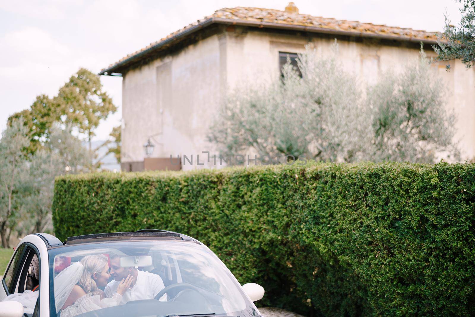 Beautiful bride and groom leaning forehead to forehead in a convertible in front of the old villa in Italy, in Tuscany, near Florence by Nadtochiy