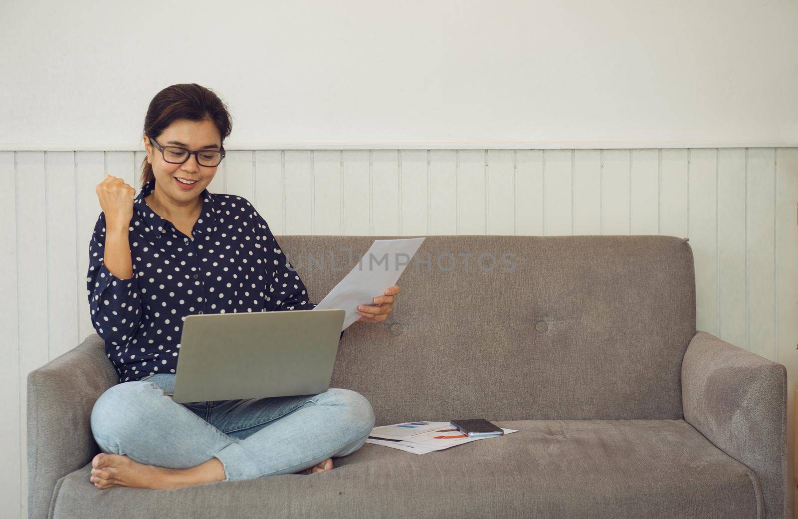 Business woman holding paperwork and video calling via laptop talk to assistant in home.She is very happy to get the order on a video meeting. Work from home concept during Coronavirus pandemic. by thanumporn