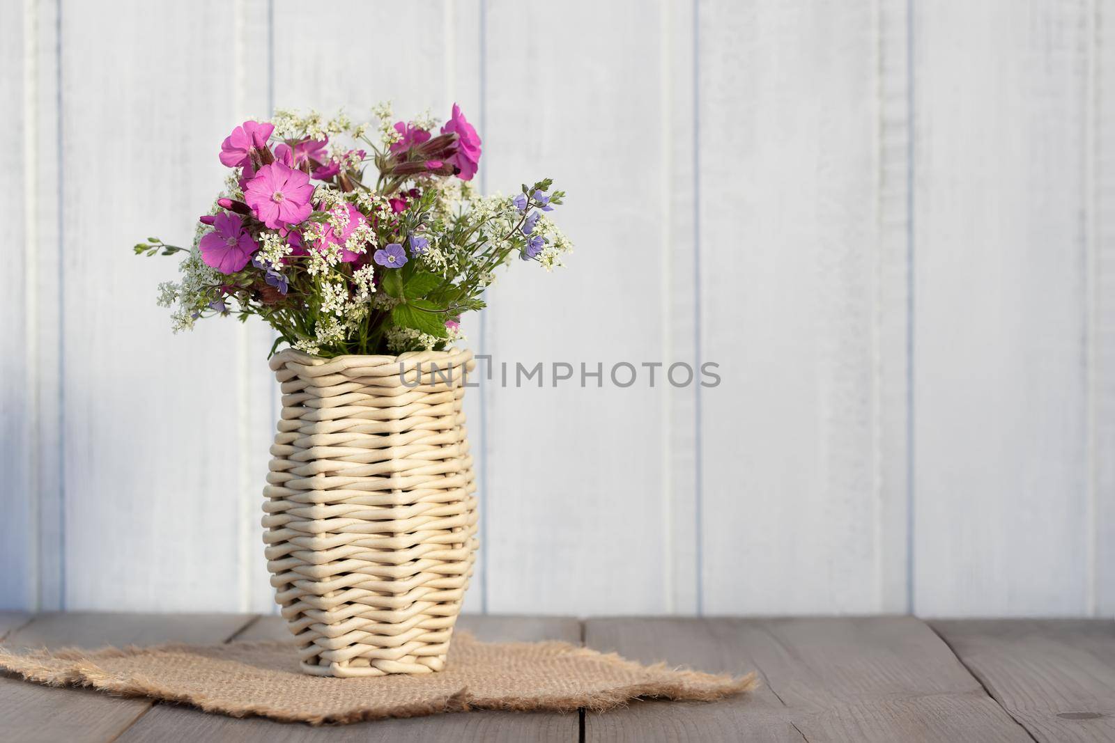 Bouquet of wildflowers in a wicker vase on a wooden table by galsand
