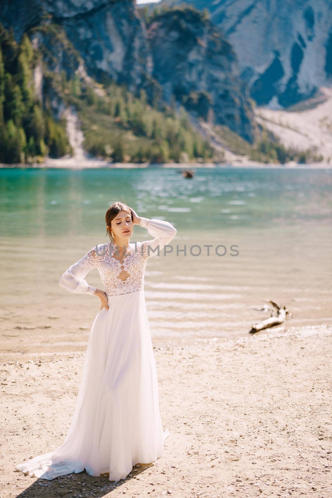 Beautiful bride in a white chiffon dress with sleeves and lace on the shore of Lake Lago di Braies in Italy. Destination wedding in Europe, on the popular Braies lake. by Nadtochiy