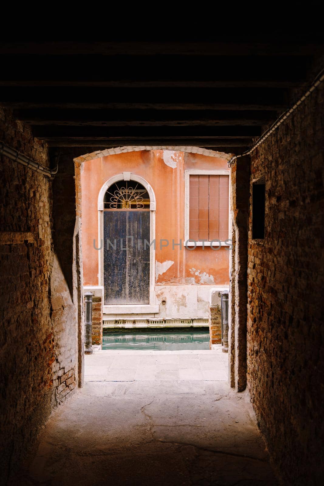 A look from the darkness at the light, at the old scratched door on the peach-colored wall near the water in the canal.