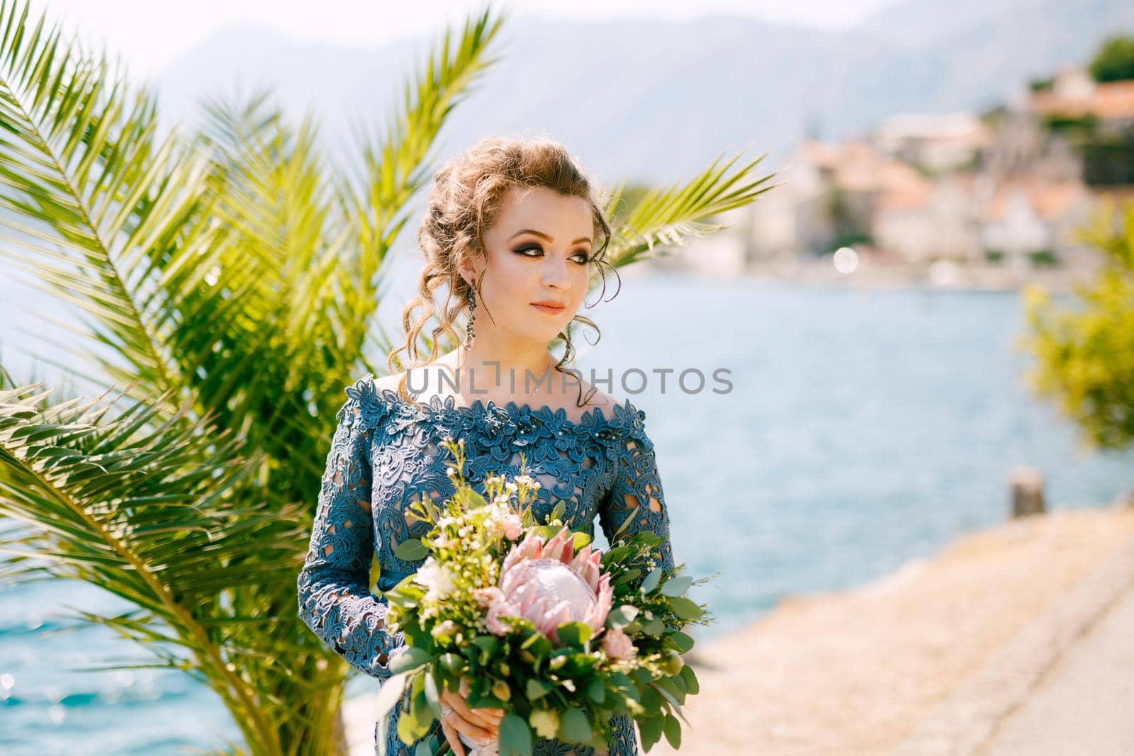 The bride in a stylish gray dress stands with wedding bouquets on the pier near old town of Perast, close-up by Nadtochiy