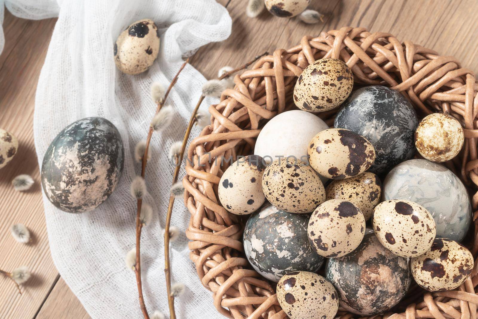 Easter composition - Easter eggs painted with natural dyes in a wicker nest on a wooden table.