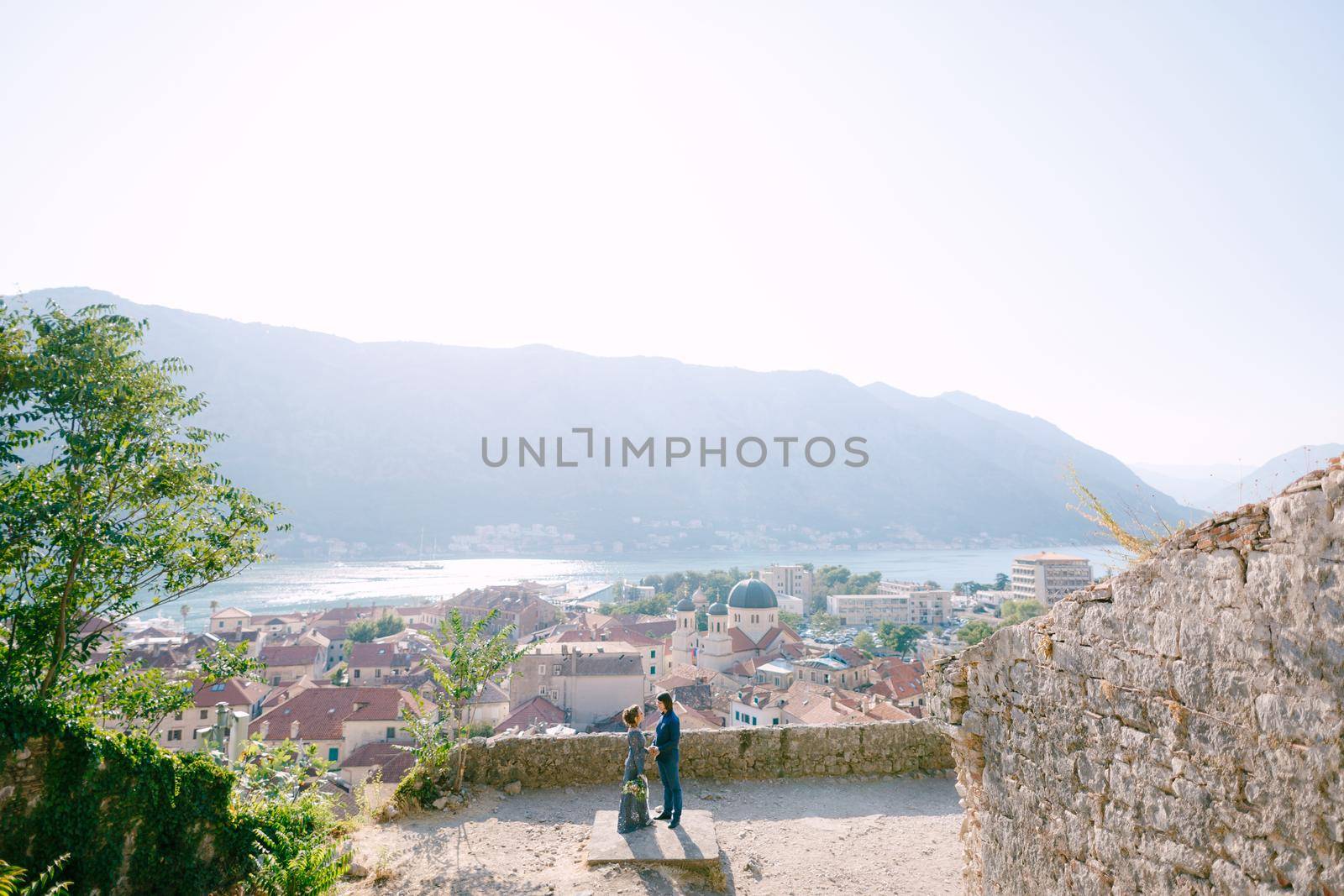 The bride and groom hug on the observation deck with a picturesque view of the old town of Kotor and the Bay of Kotor . High quality photo