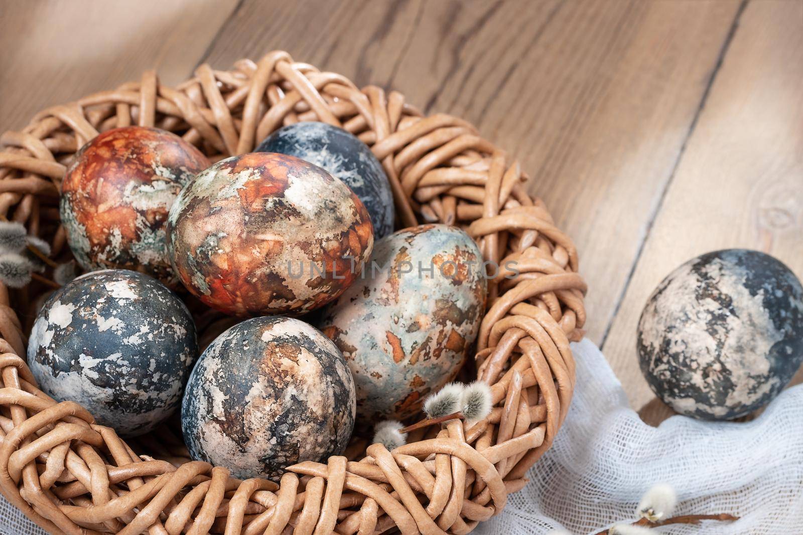 Easter composition - Easter eggs painted with natural dyes in a wicker nest on a wooden table by galsand