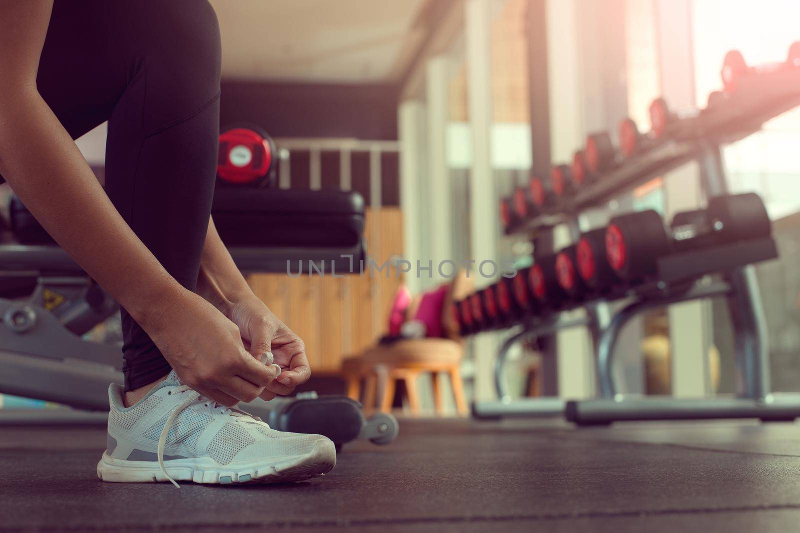 Close up of woman's hands tying shoelaces on sneakers in the gym. by thanumporn