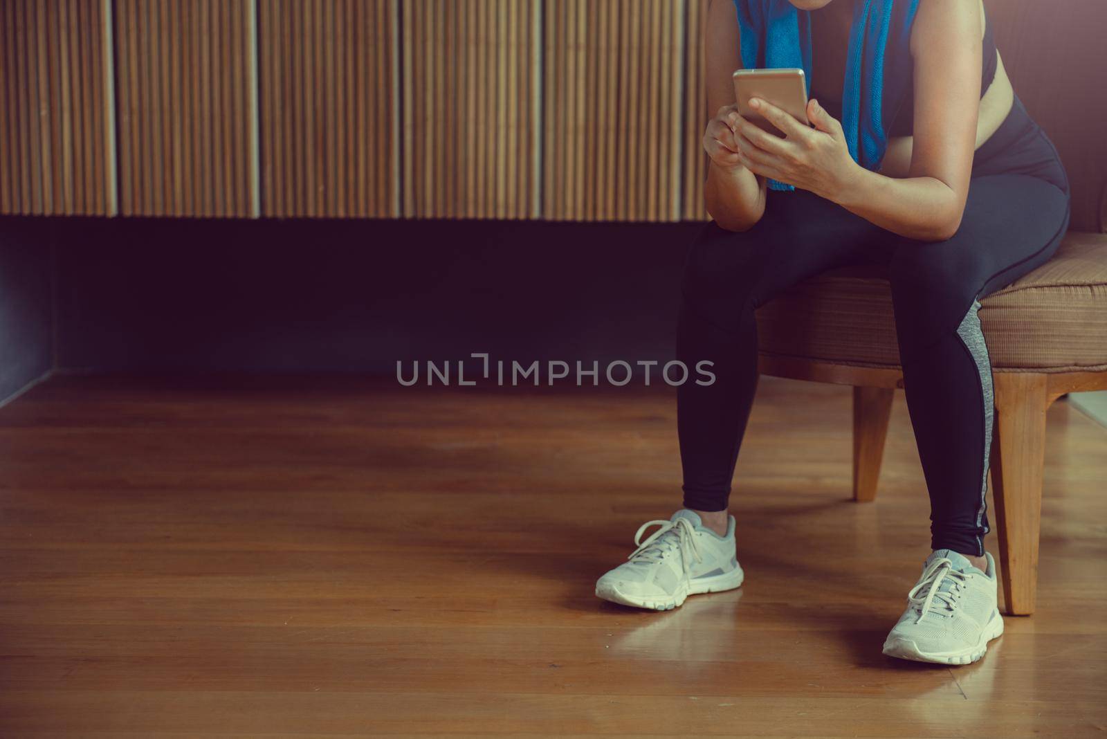 Sportswoman sitting and using smartphone in locker room at gym. by thanumporn