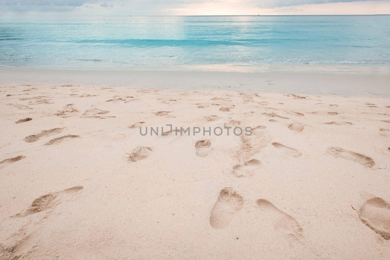 Footprints on beautiful sandy beach and turquoise sea water at sunset time. by thanumporn