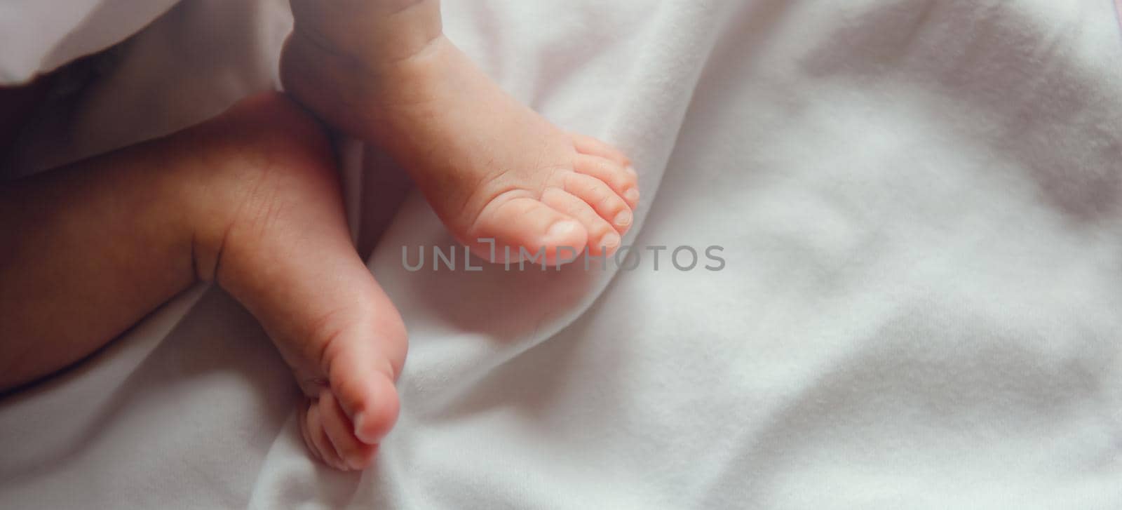 Close-up tiny newborn baby feet on a white blanket.