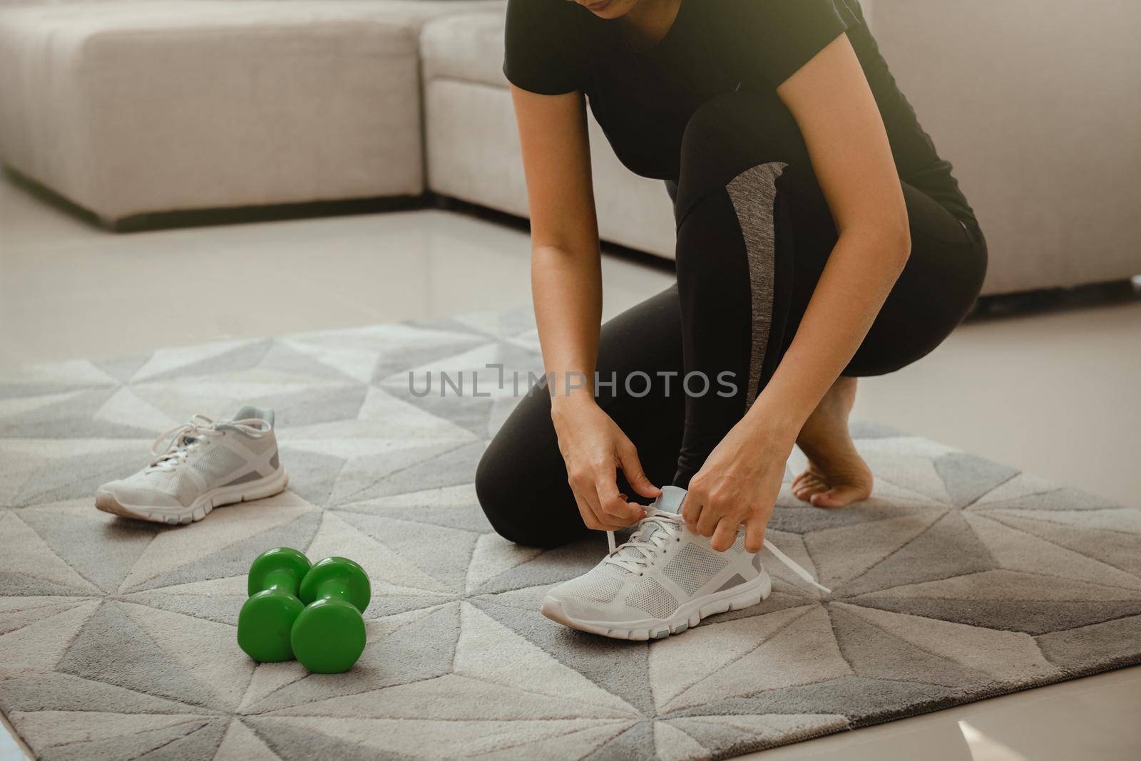 Woman getting ready for workout at home. She is tying shoelace on sneakers. Sport and recreation concept.