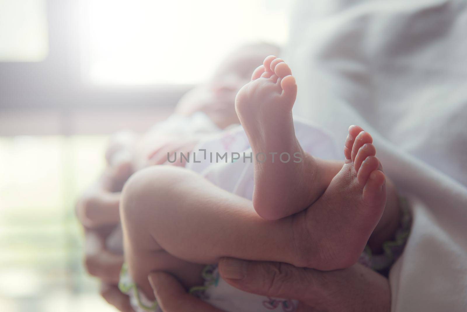 Parent is holding small infant. Baby's foot is in focus. by thanumporn