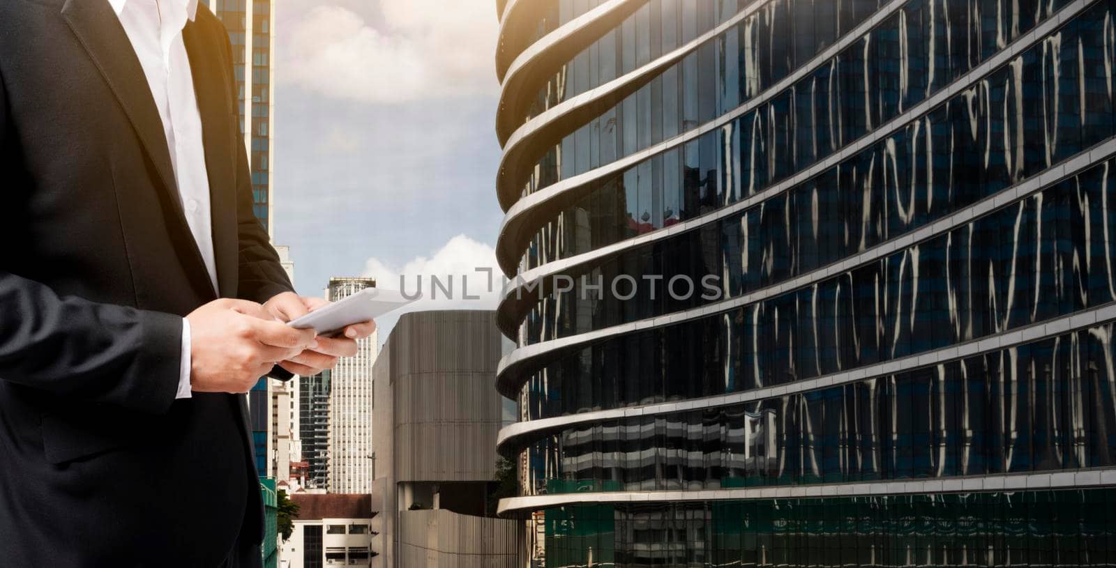 Businessman working online with a digital tablet with office building background. by thanumporn