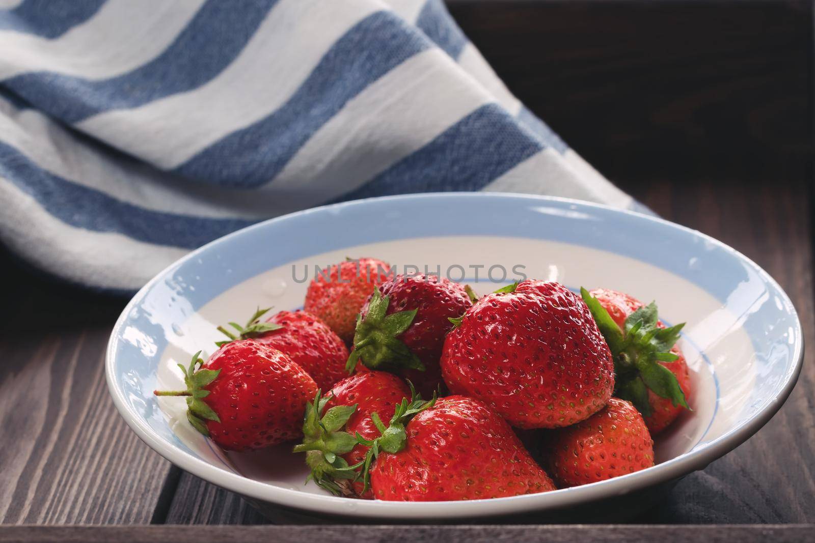 Natural ripe strawberries in a plain white bowl on a dark wooden table.