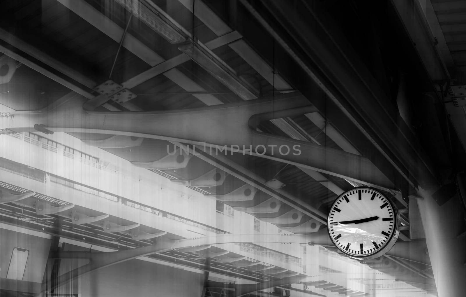 The clock shows the time on the skytrain station with iron structure roof background. Toned Monochrome. by thanumporn