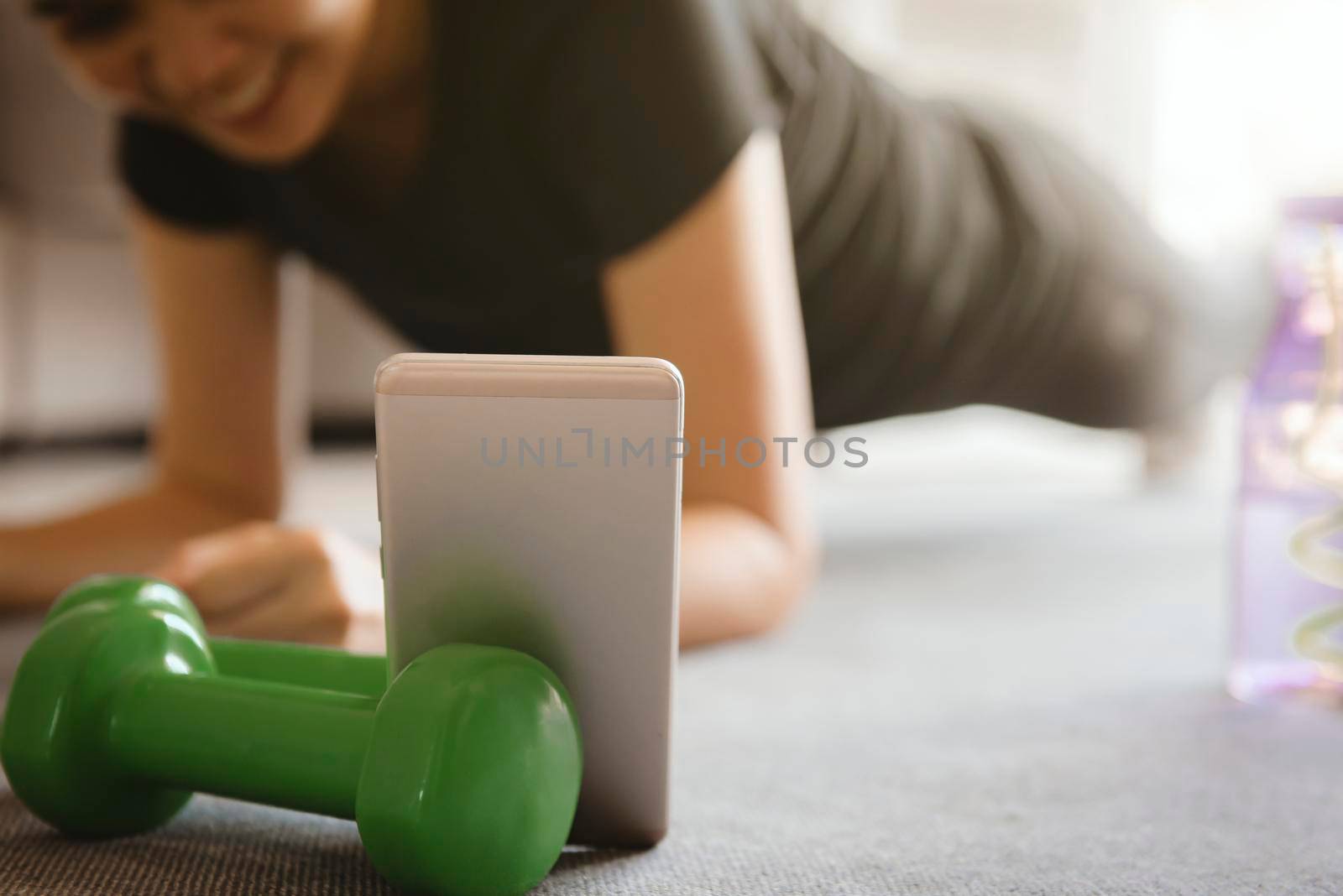 A sporty woman using smartphone during workout at home in the living room. Online personal trainer or on mobile phone.Sport and recreation concept. by thanumporn
