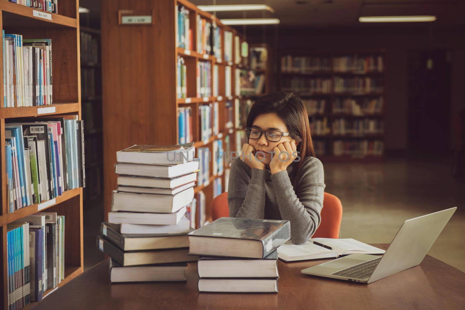 Bored young female student sitting at table in a campus open space library. Education concept by thanumporn