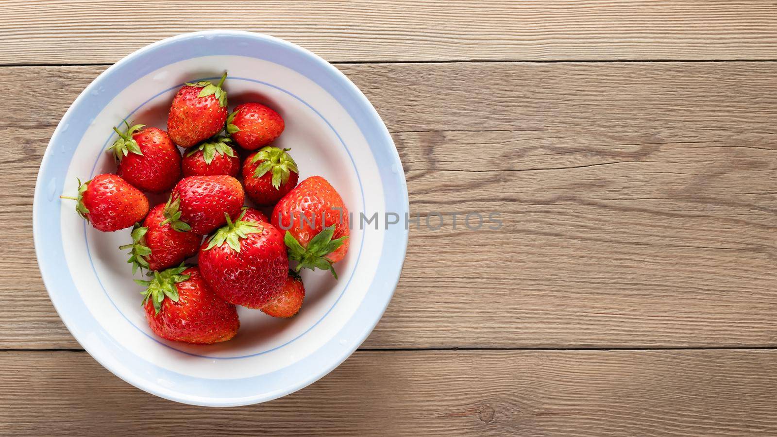 Natural ripe strawberries in a plain white bowl on wooden background. Top view, copy space by galsand