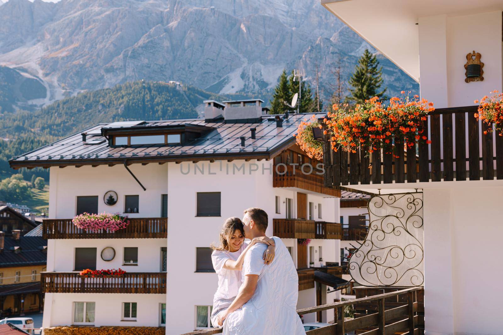 A guy and a girl cuddle with a blanket outside a hotel in mountains. Cortina Ampezzo is an Italian city in province of Belluno in Veneto region, a winter resort in Dolomites