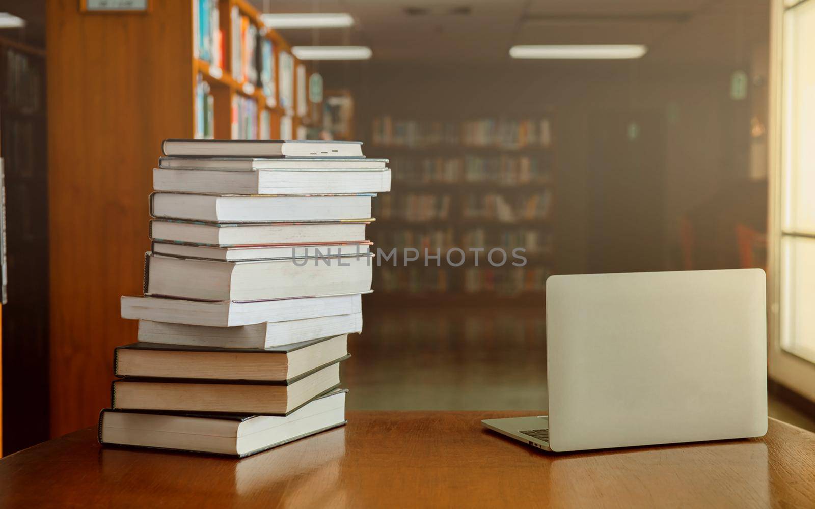 Stack of old books and laptop computer on desk in library background. Educational technology concept.