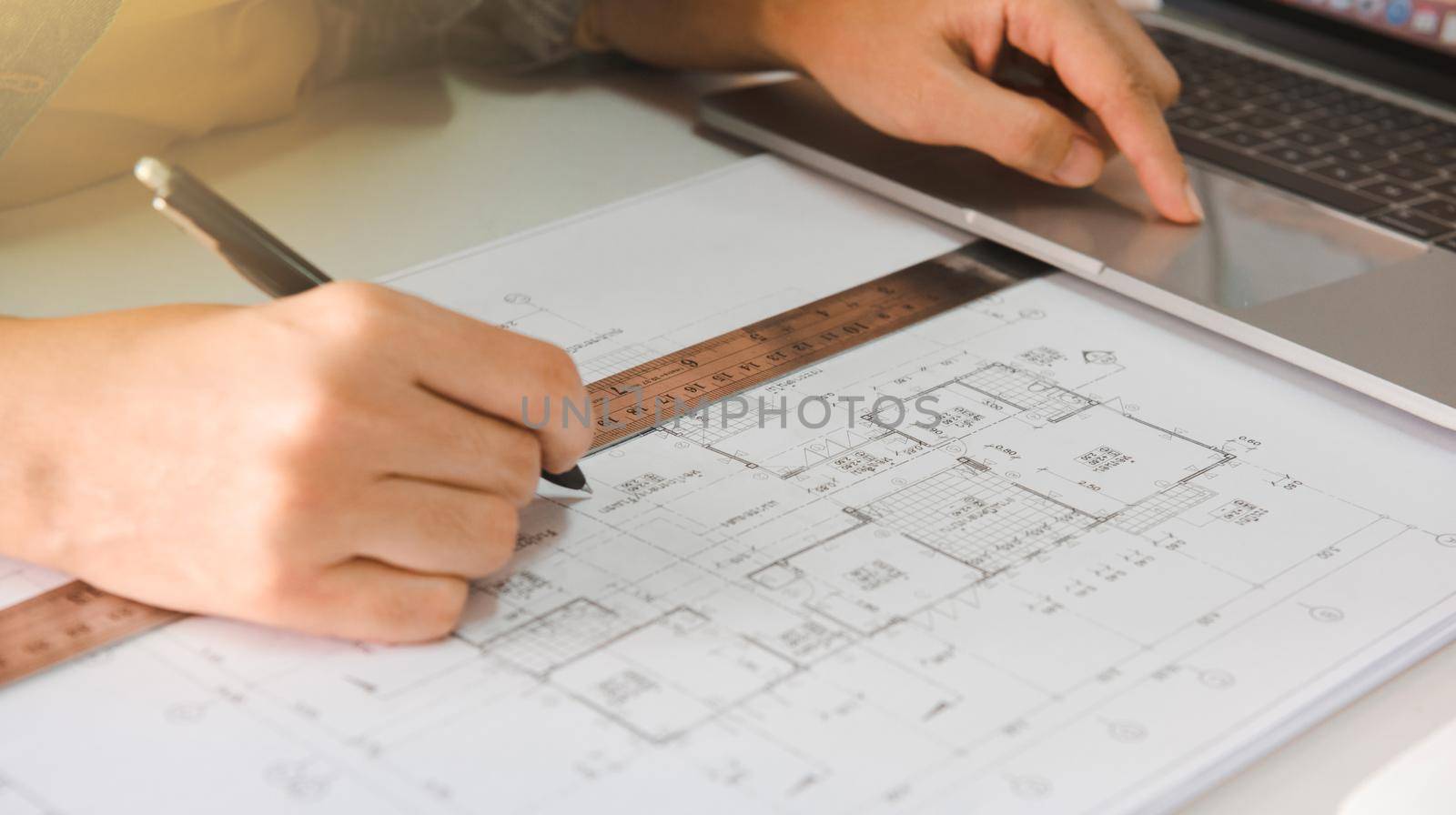 Engineers holding a pen pointing to a building and using laptop to planning project schedule. Engineering and construction concept.