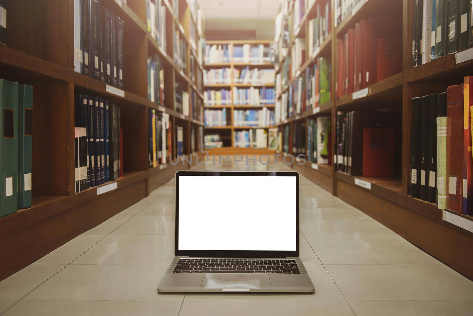 Laptop with blank screen on floor. interior background, bookshelf, library.Educational technology concept. by thanumporn