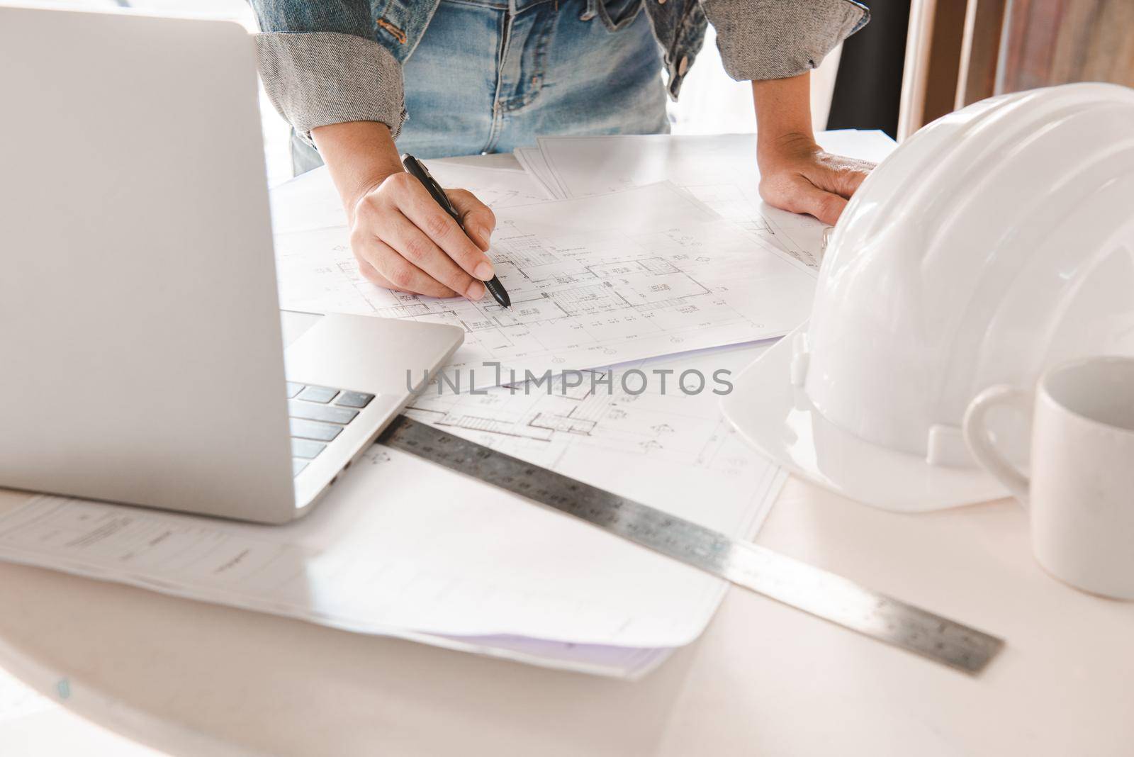 Engineers holding a pen pointing to a building and using laptop to planning project schedule. Engineering and construction concept.