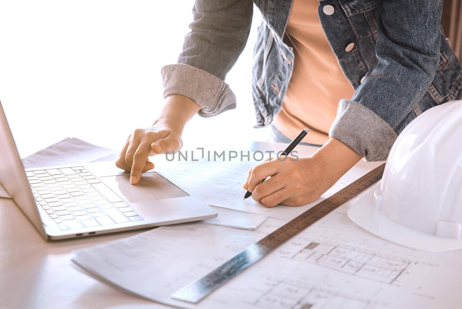 Engineers holding a pen pointing to a building and using laptop to planning project schedule. Engineering and construction concept.