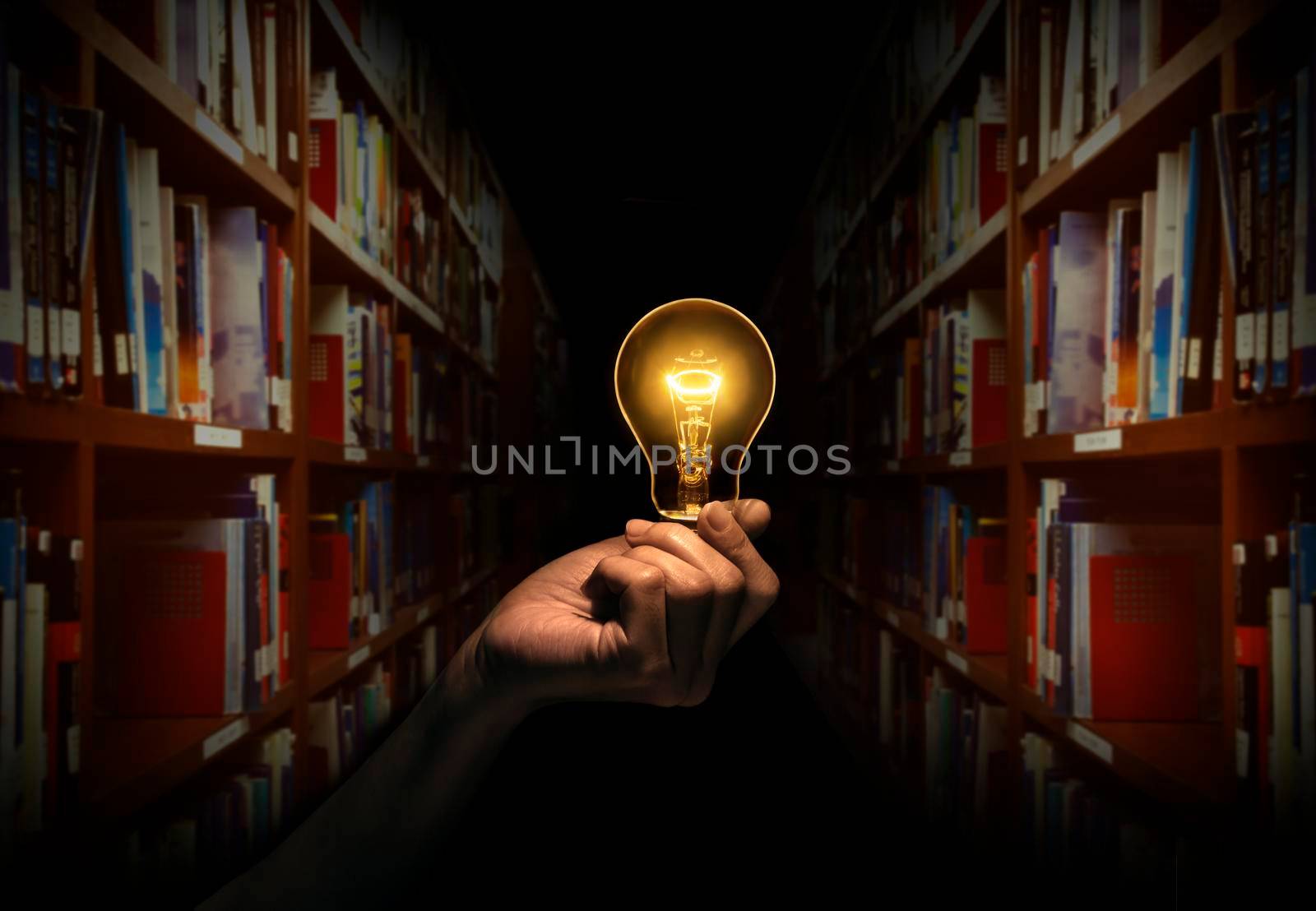 Hand holding a light bulb with bookshelf in library background. Concept The idea of reading books, knowledge, and searching for new ideas. by thanumporn