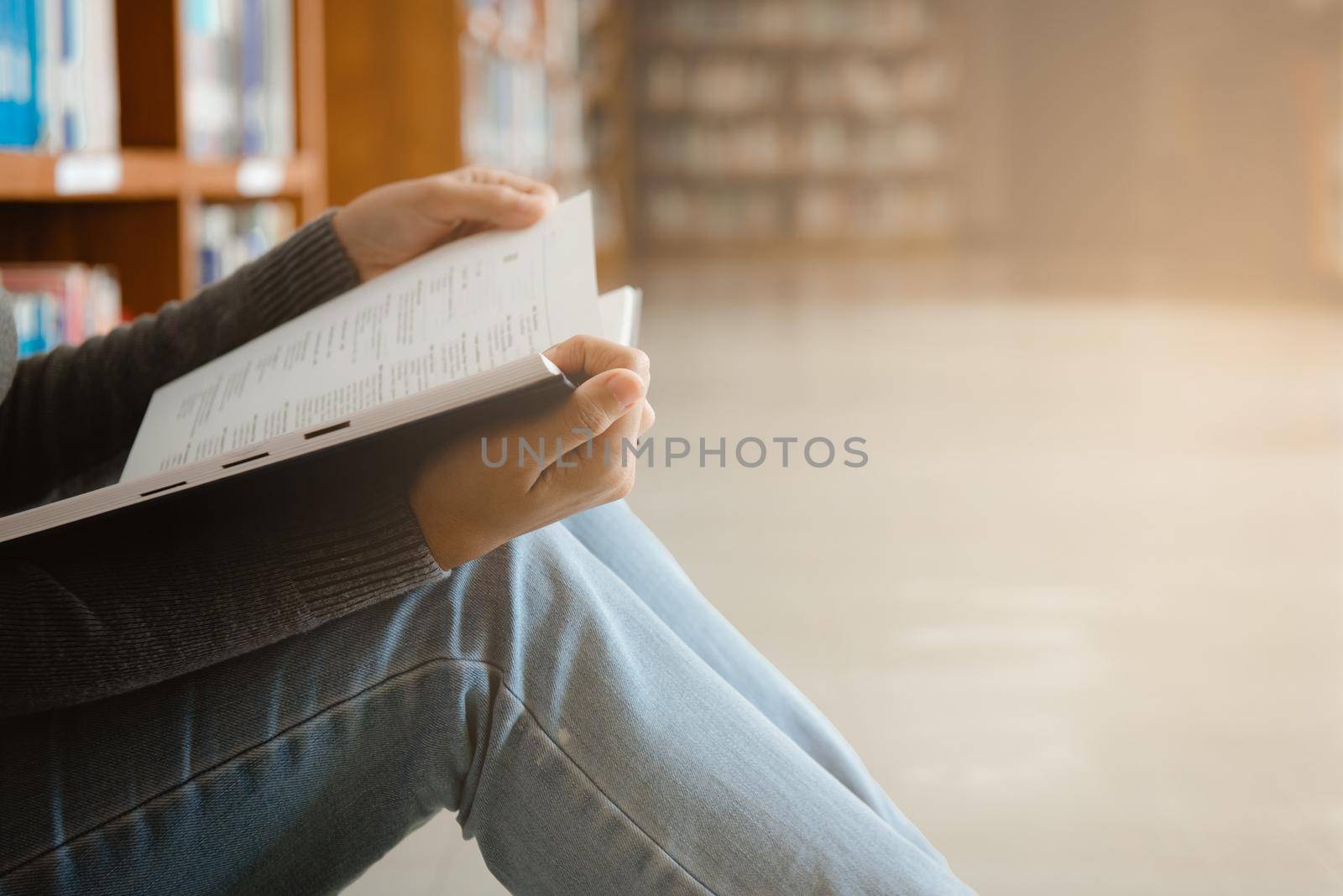 Close-up of an asian woman reading an old book in the corner of a university library. With golden light shining through the glass of the room by thanumporn