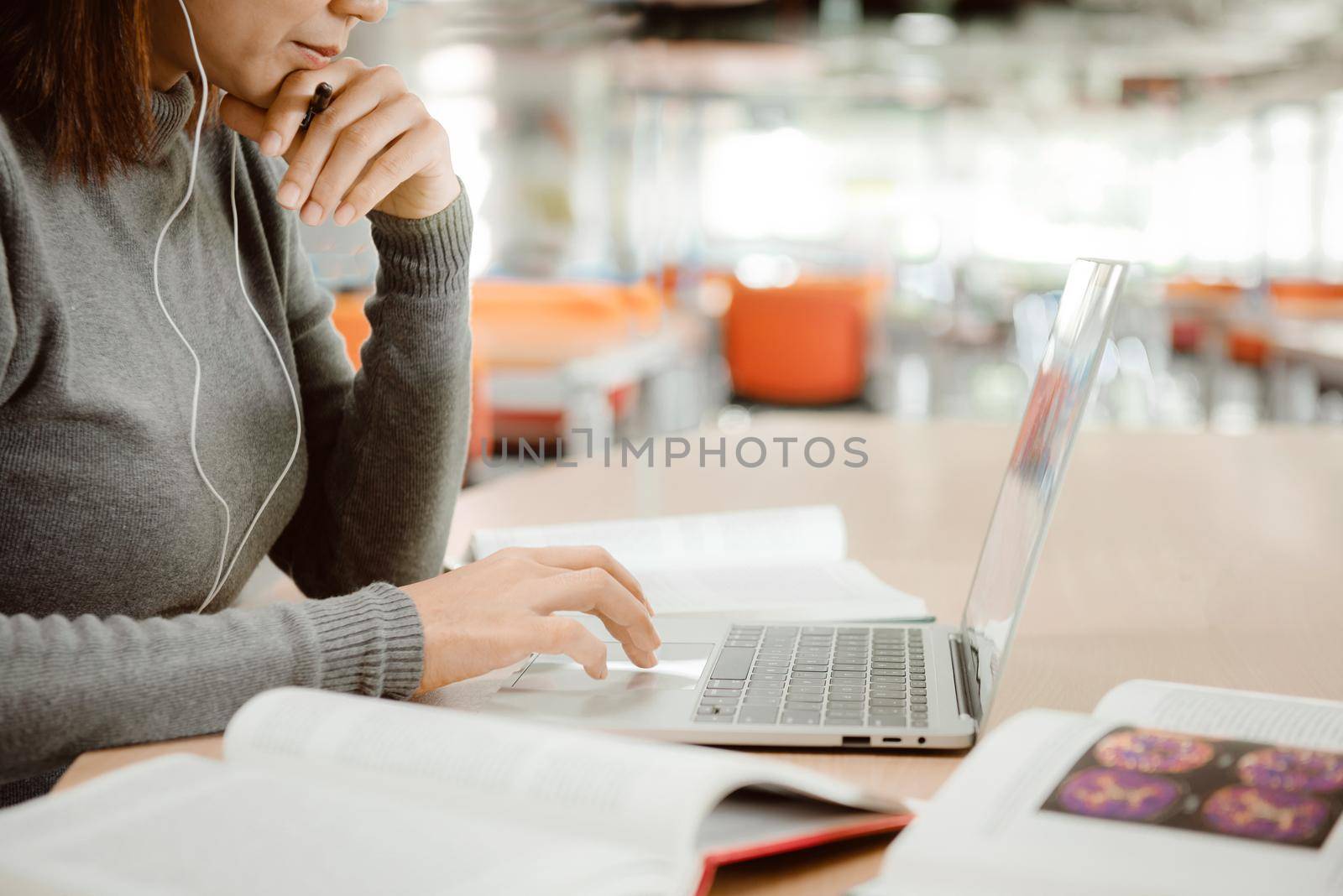 A girl student with headphones preparing for examination and using laptop while sitting at table at university library.