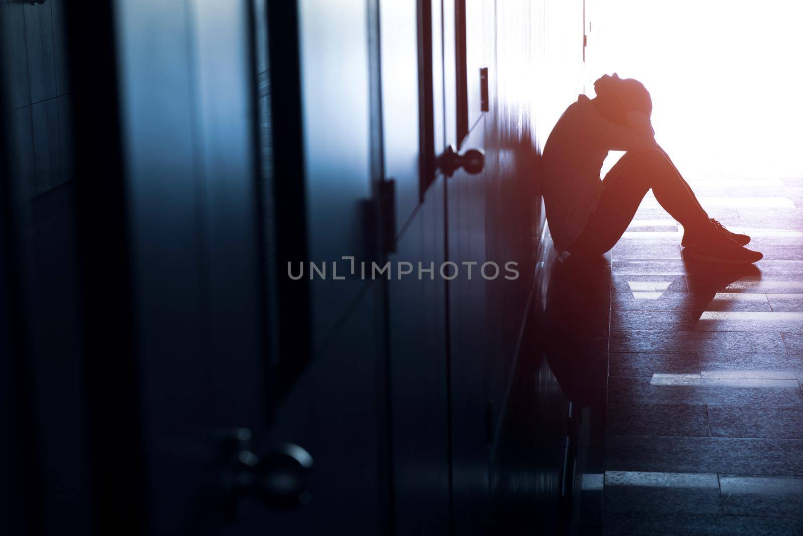 Silhouette of depressed man sitting on walkway of building. Sad man, Cry, drama, lonely and unhappy concept. by thanumporn