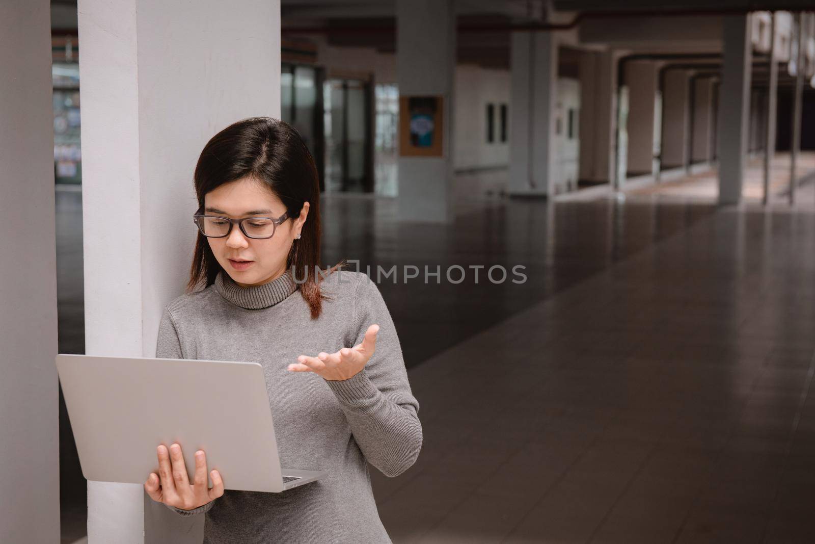 Woman in office has video conversation. Young positive woman in glasses standing in front of laptop and talking with somebody online.