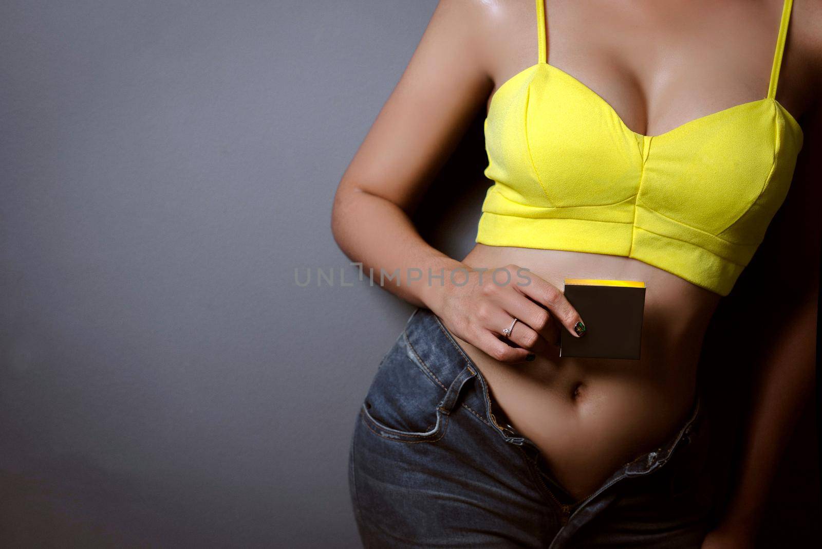 Young woman holding a blackbox in yellow singlet and jeans texas shorts on dark background.