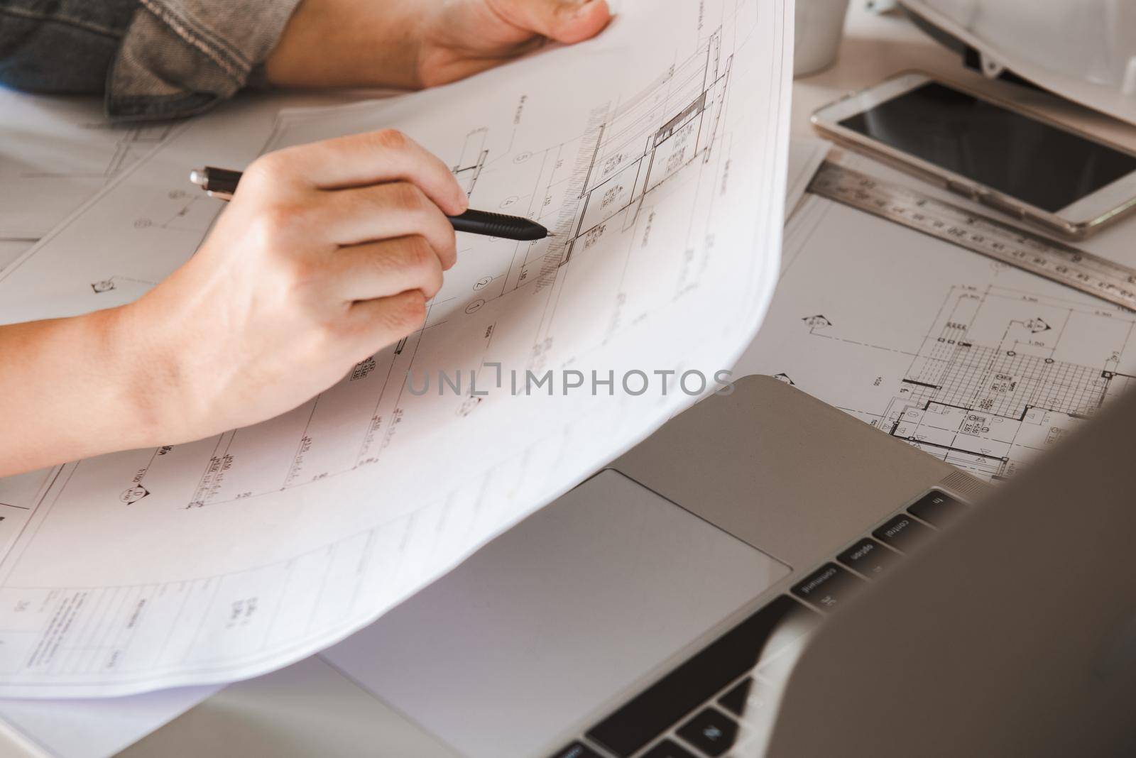 Engineers holding a pen pointing to a building on a blueprint and using a computer laptop to planning project schedule. Engineering and construction concept.