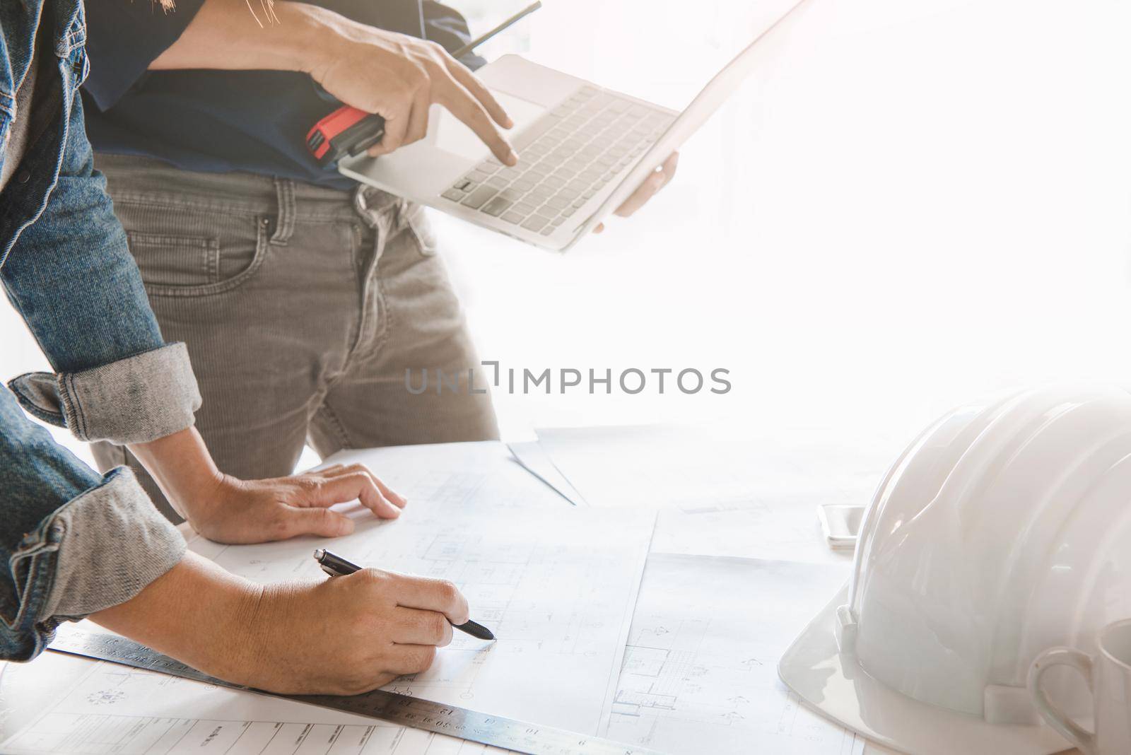 Engineer are discuss planning to drawing house structure on Blueprint and design graphic model house on laptop computer for his customers.Engineering and construction concept. by thanumporn