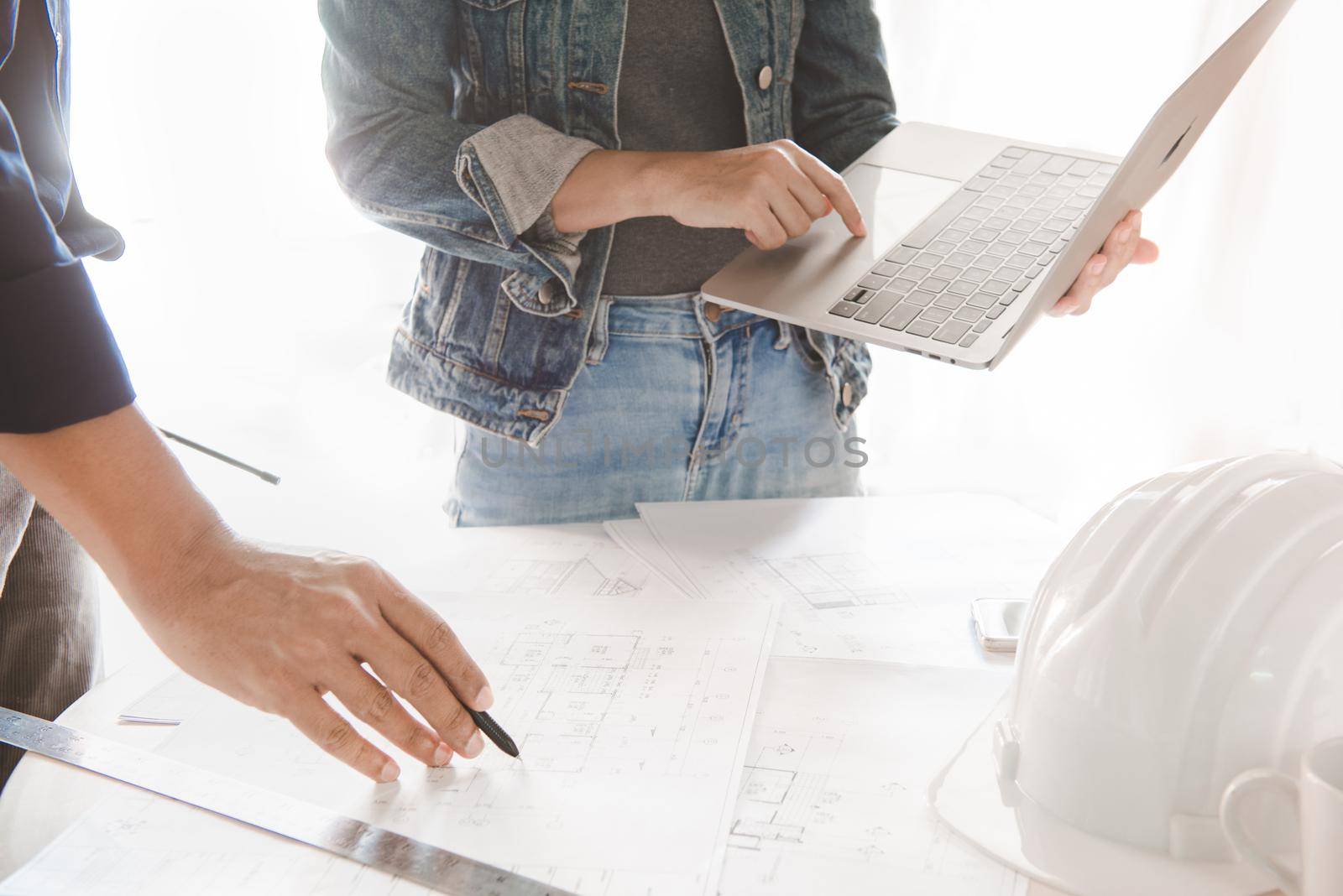 Engineer or architect working and discussing with blueprint and holding pencil and laptop on hand in office. concept of teamwork and partnership.